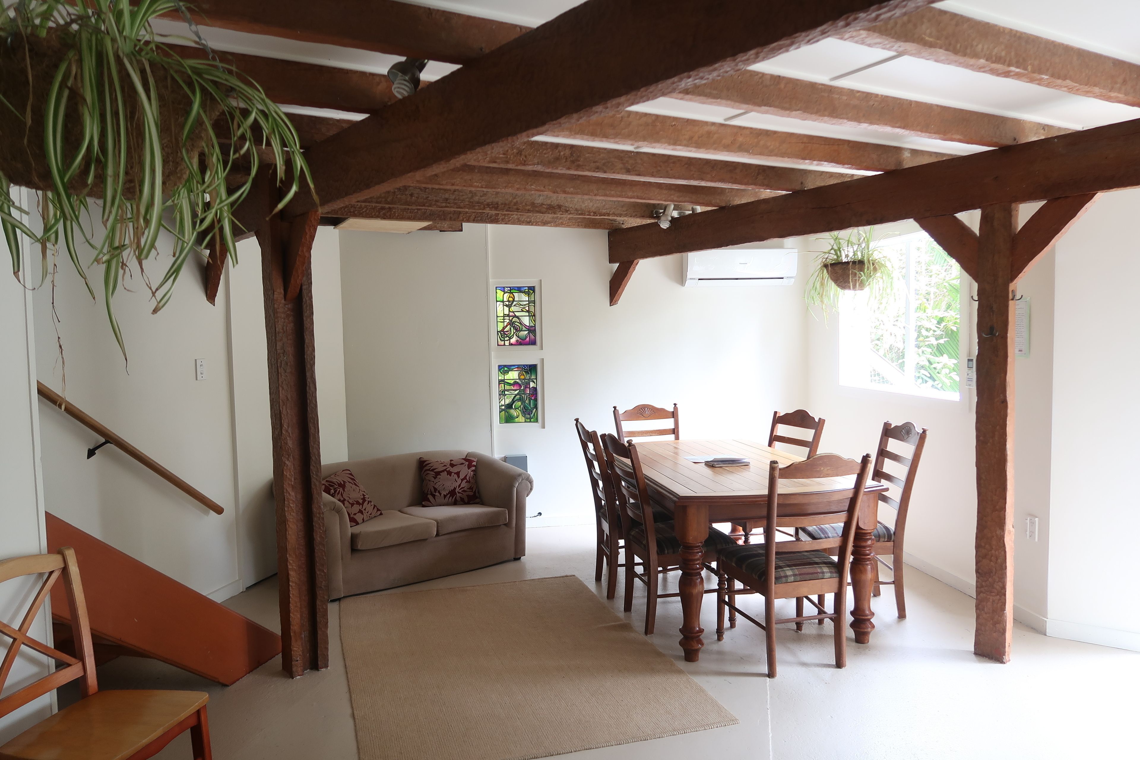 Een eetgedeelte met een houten tafel en stoelen, een bank en een hangplant.