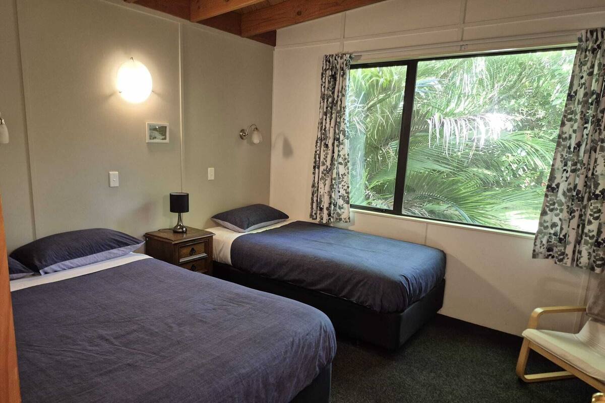 A room with two beds, a nightstand with a lamp, a chair, and a window with curtains.