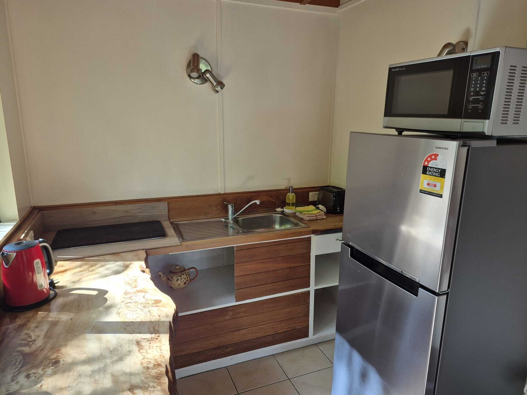 Uma cozinha compacta com micro-ondas, geladeira de aço inoxidável, pia e bancada de madeira.
