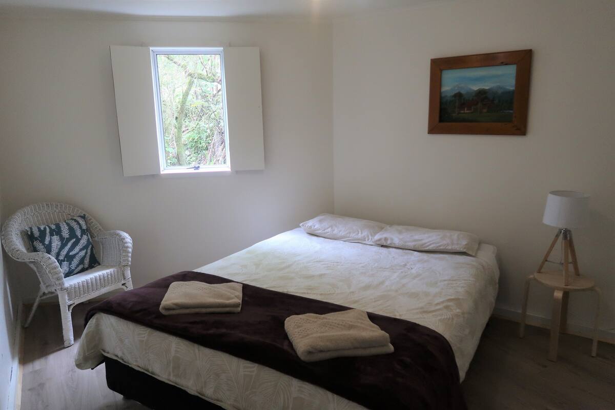 A bedroom with a bed, a chair, a window, a painting, and a lamp.