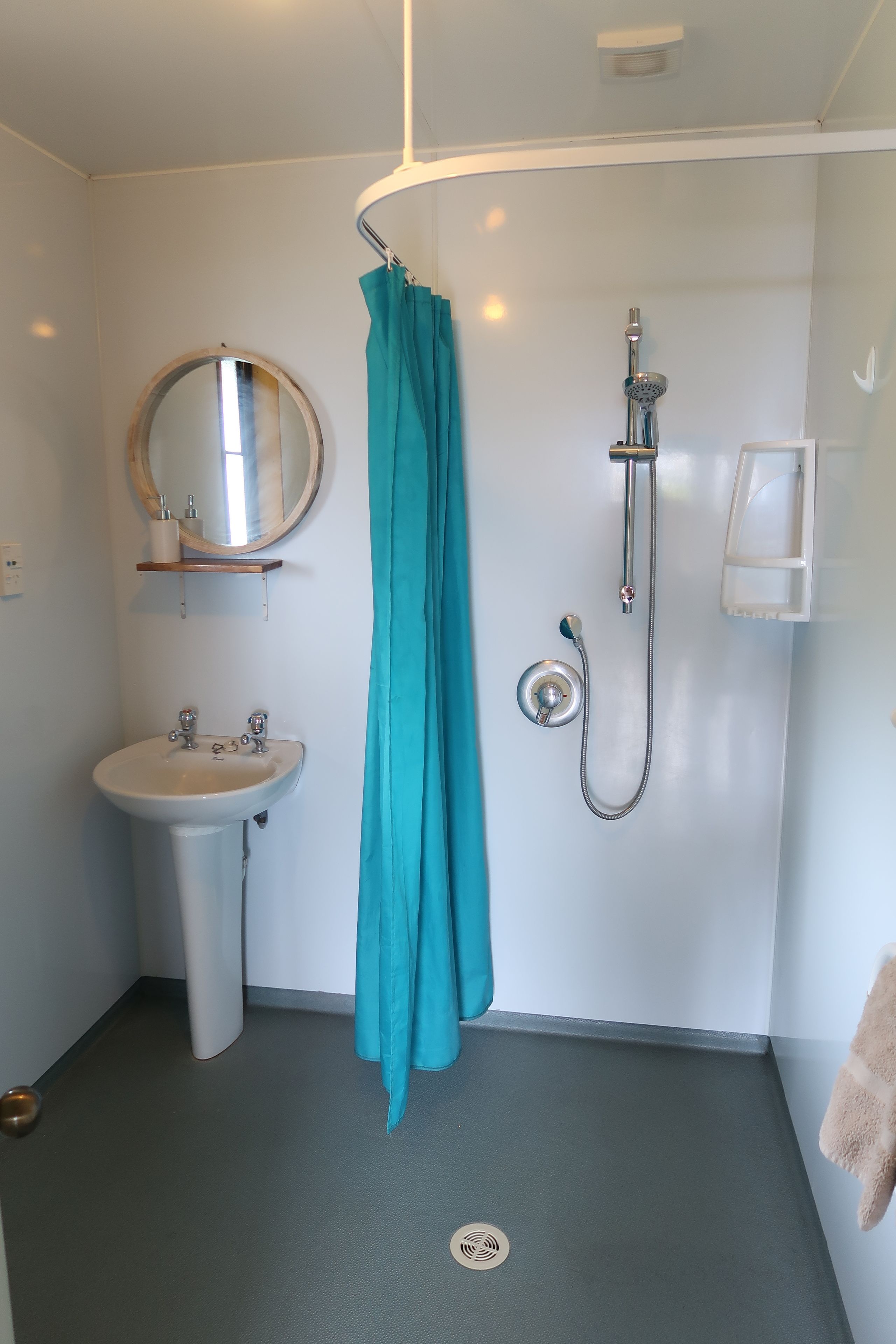 Baño con lavamanos, espejo, ducha y toallero.