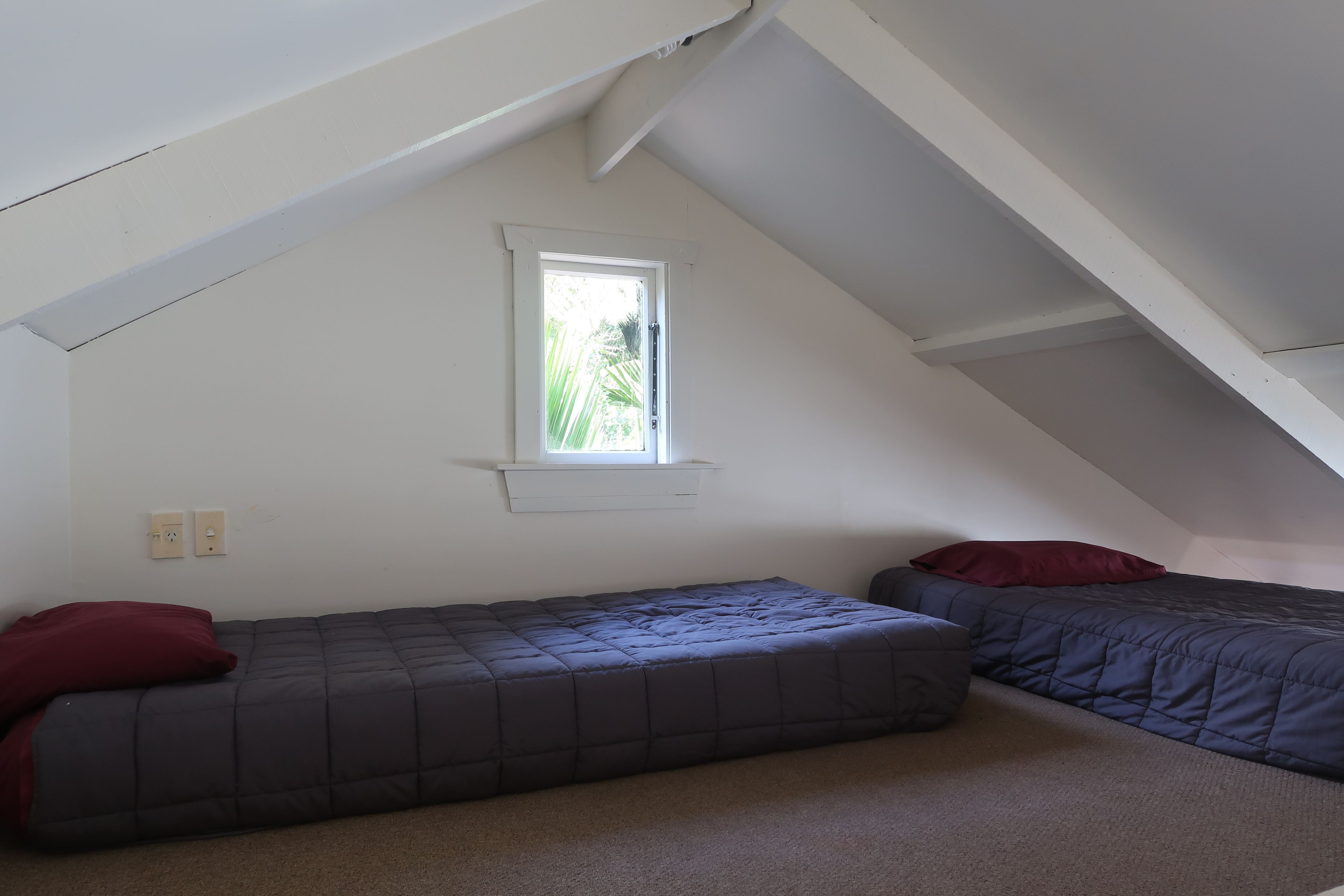 A small, dimly lit attic bedroom with two single beds, a window, and a sloped ceiling.