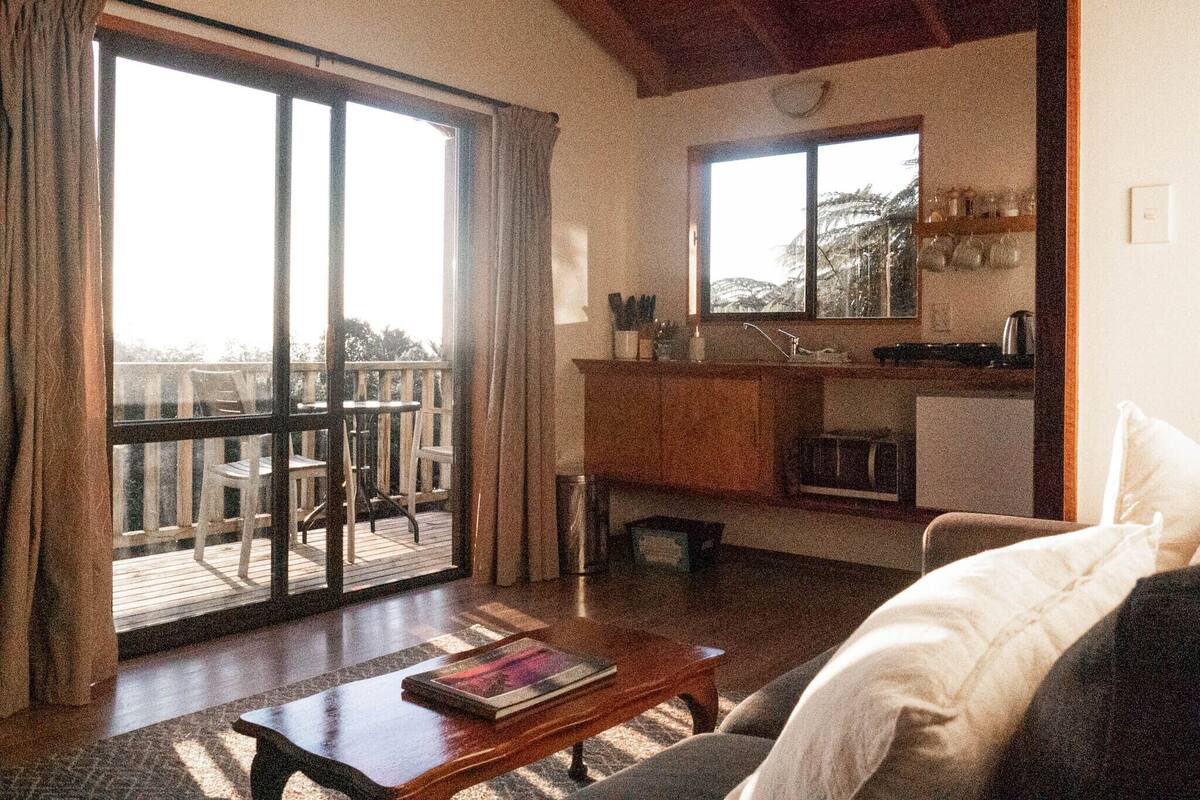 A cozy living room with a sofa, a coffee table, and a sliding glass door leading to an outdoor deck.