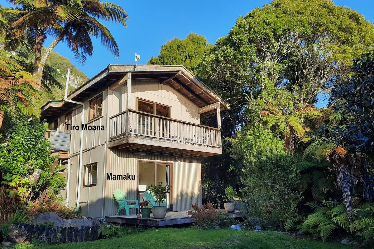 A two-story house with a balcony, surrounded by lush greenery and trees.