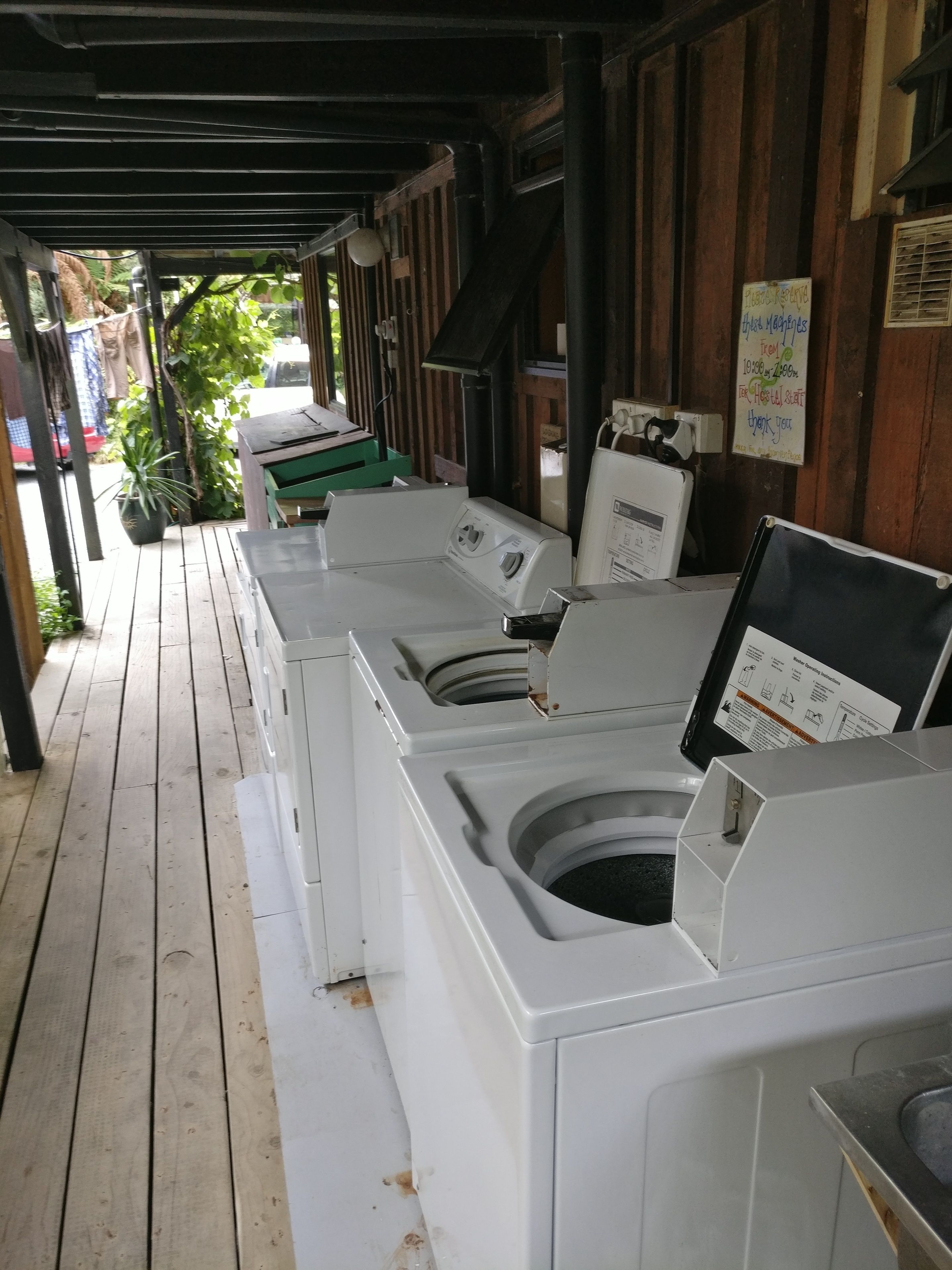 A row of white laundry machines under a wooden structure with a signboard.