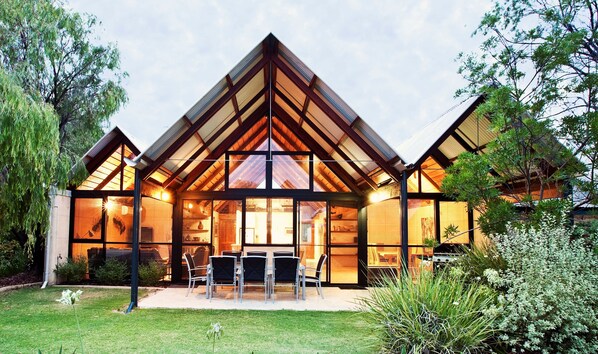 A modern house with a large glass facade, a wooden roof, and a patio with outdoor seating.