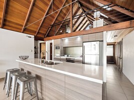 Una cocina moderna con techo de madera, una isla grande con taburetes de bar y vistas al área de estar contigua.