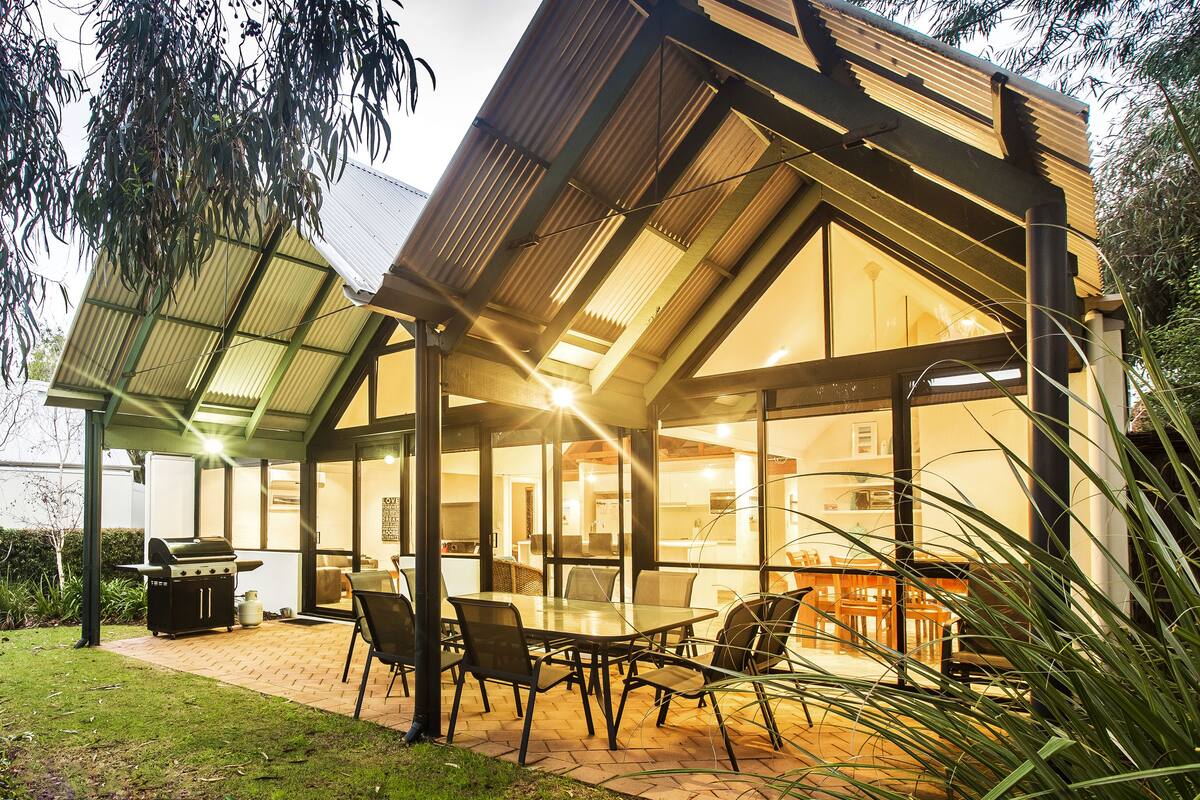 A modern house with a covered patio, a barbecue, and a dining area with chairs and a table.