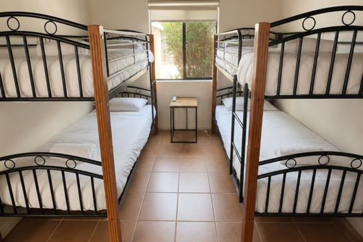 A dormitory room with bunk beds, a small table, and a window.