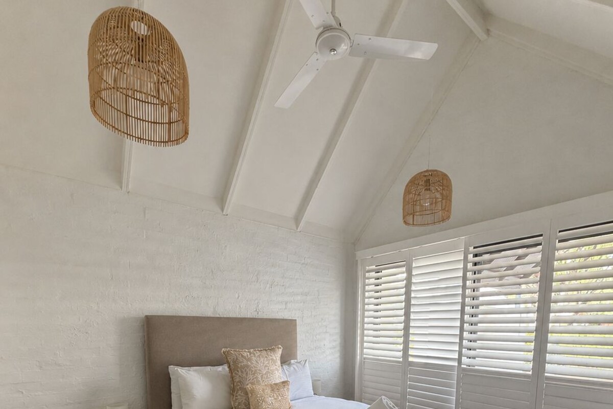 A bedroom with a large bed, a ceiling fan, and a window with blinds.