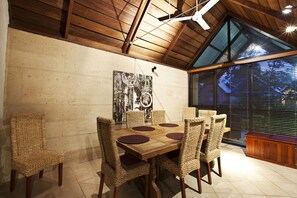 A dining area with a wooden table and woven chairs, a ceiling fan, and a large window with blinds.