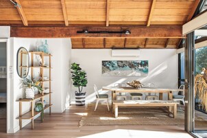 Un interior moderno con techo de madera, un comedor con mesa y sillas, un ventanal grande y un equipo de aire acondicionado instalado en la pared.