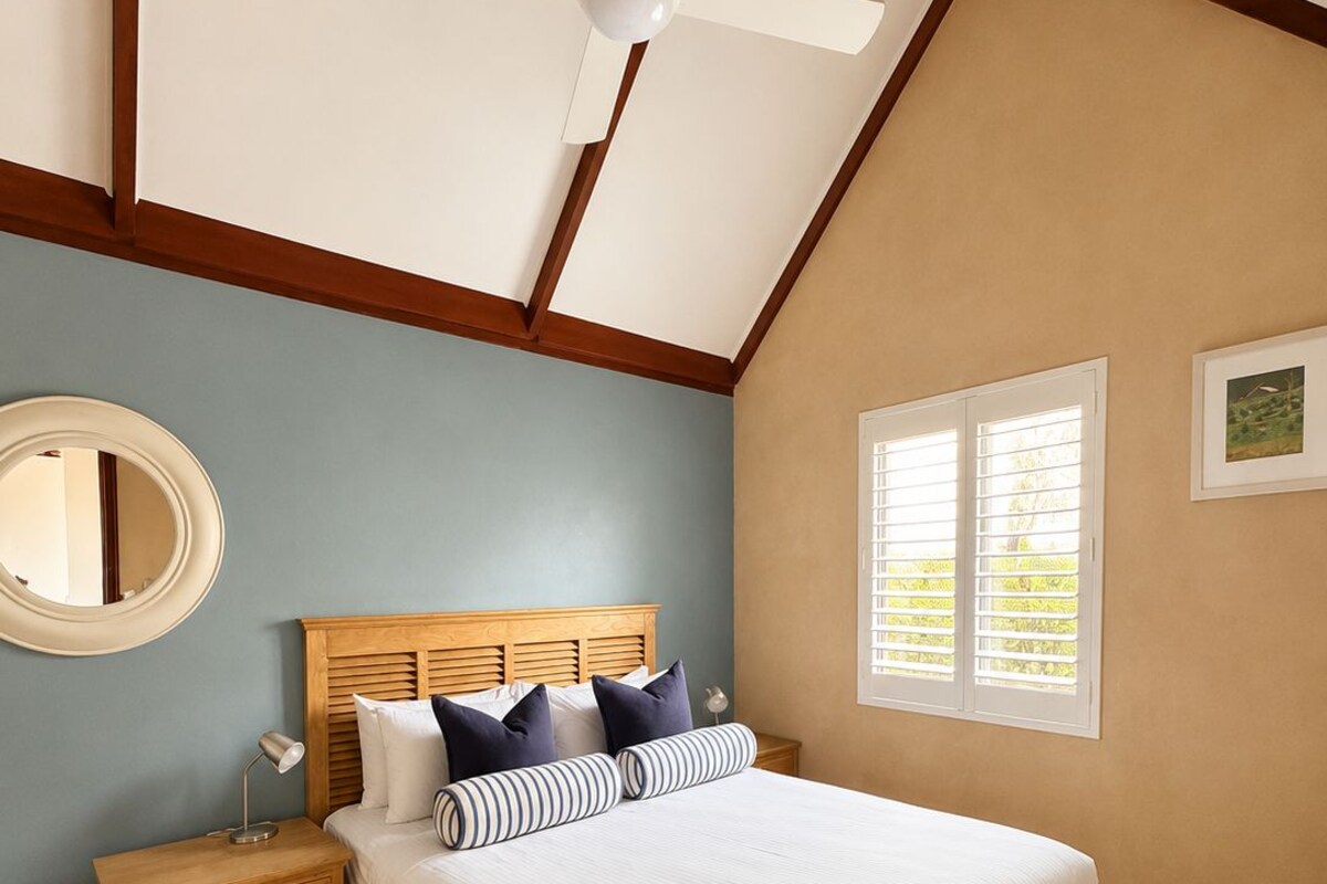 A bedroom with a bed, a nightstand, a mirror, a ceiling fan, and a window with blinds.
