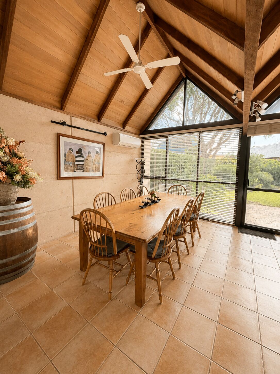 A dining area with a wooden table and chairs, a ceiling fan, and a large window with blinds.