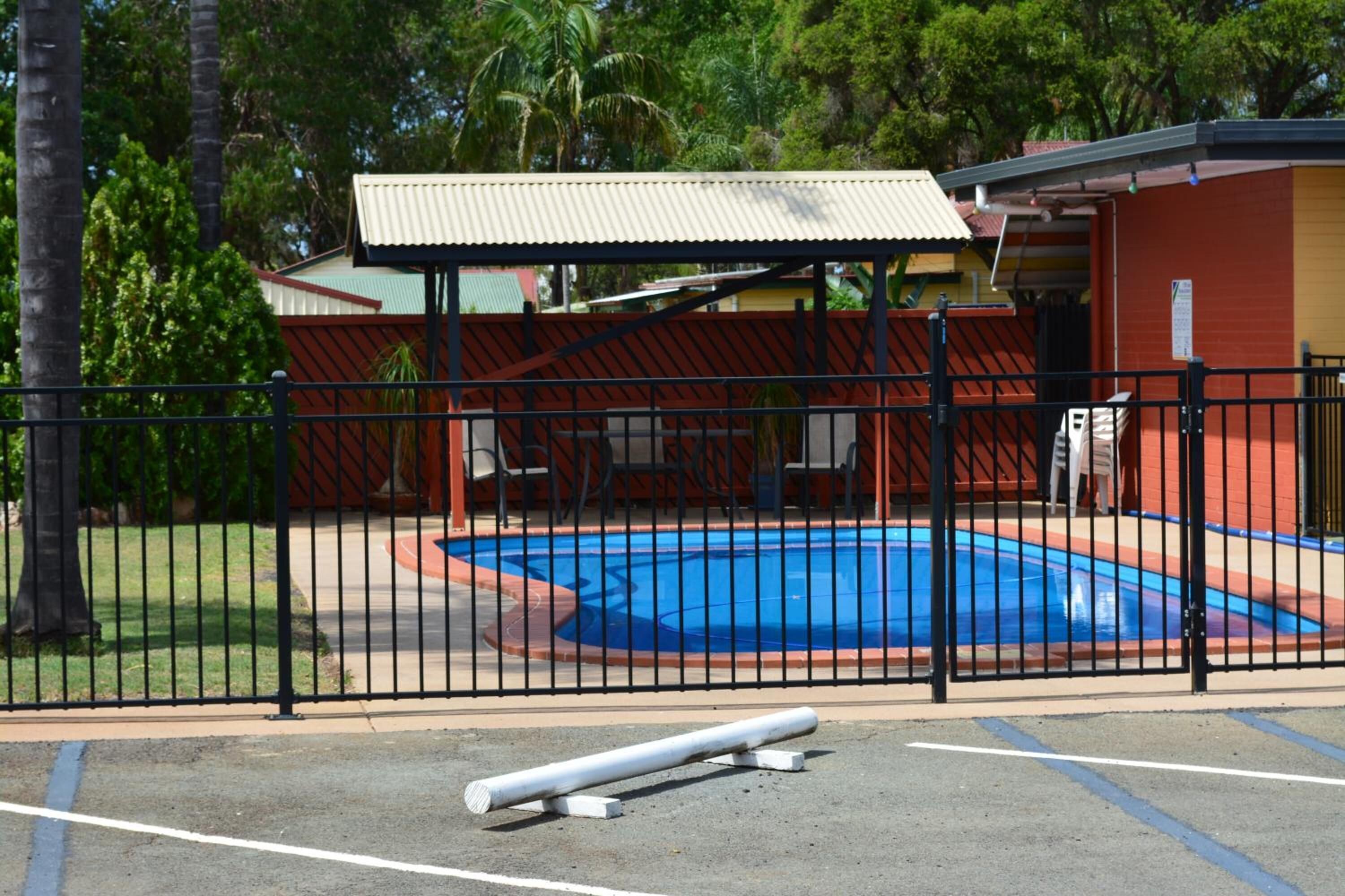 A fenced swimming pool area with a covered structure, surrounded by a building with a red and yellow facade.
