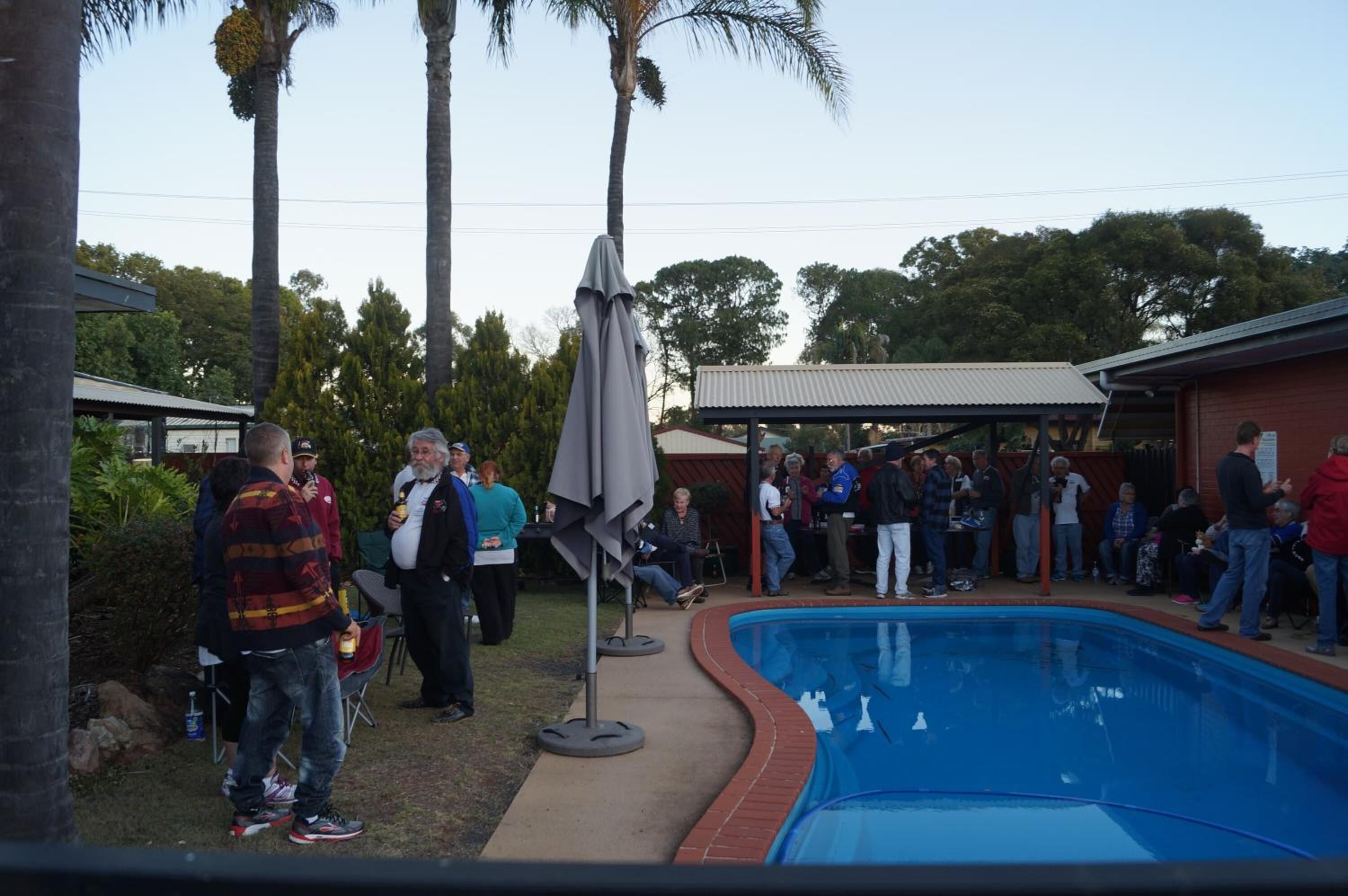 Une réunion conviviale au bord de la piscine, avec des personnes assises autour de la piscine et dans un espace abrité.