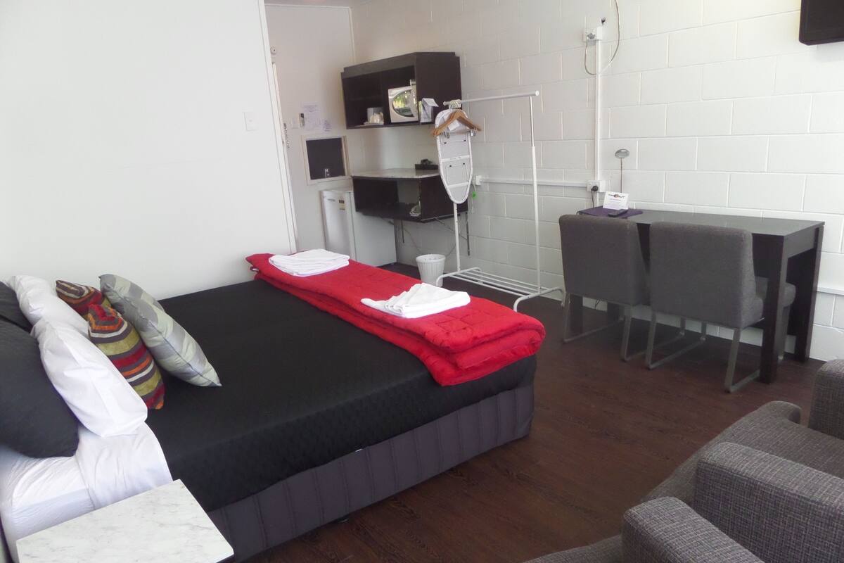 Una habitación pequeña con cama, escritorio y dos sillas.