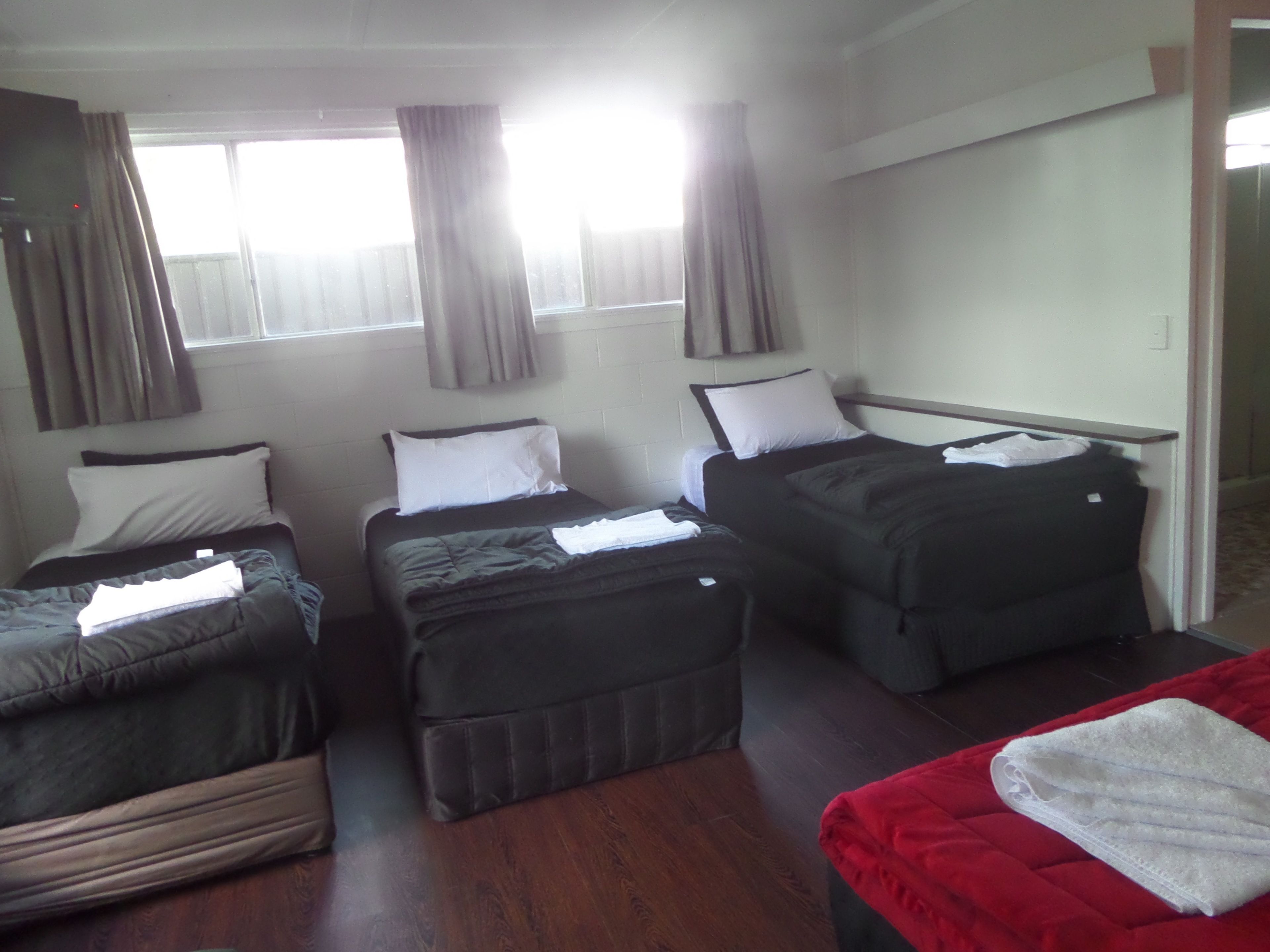 Habitación de hotel con tres camas individuales, una cama roja en primer plano y suelo de madera.
