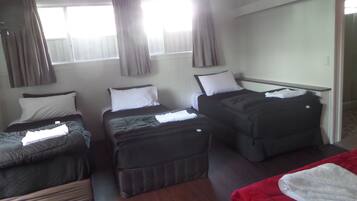 Habitación de hotel con tres camas individuales, una cama roja en primer plano y suelo de madera.