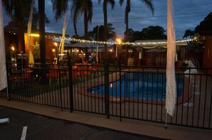 Un área de piscina con cerramiento, palmeras y luces colgantes.