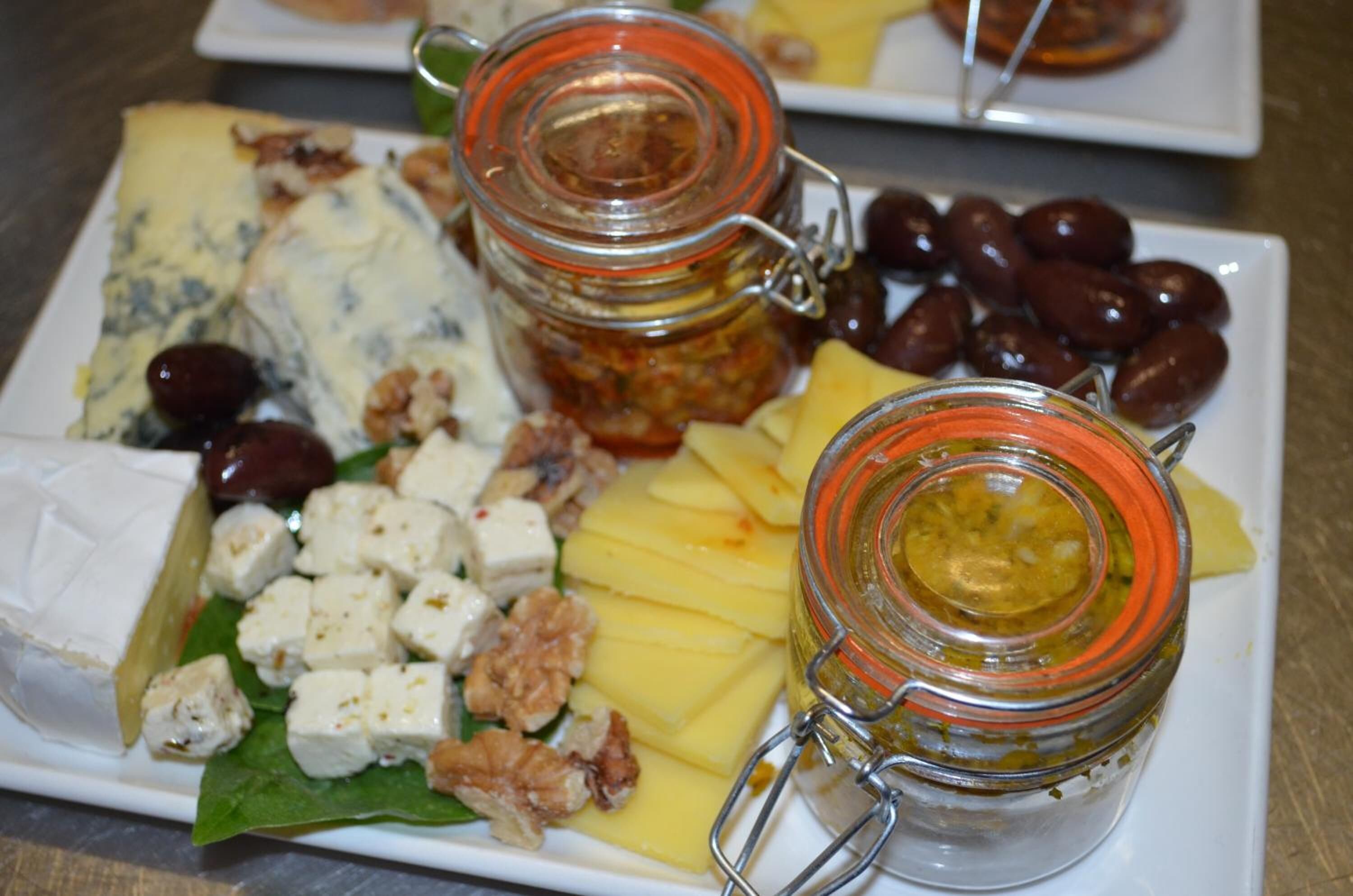 A cheese platter with various cheeses, nuts, and olives on a white plate.