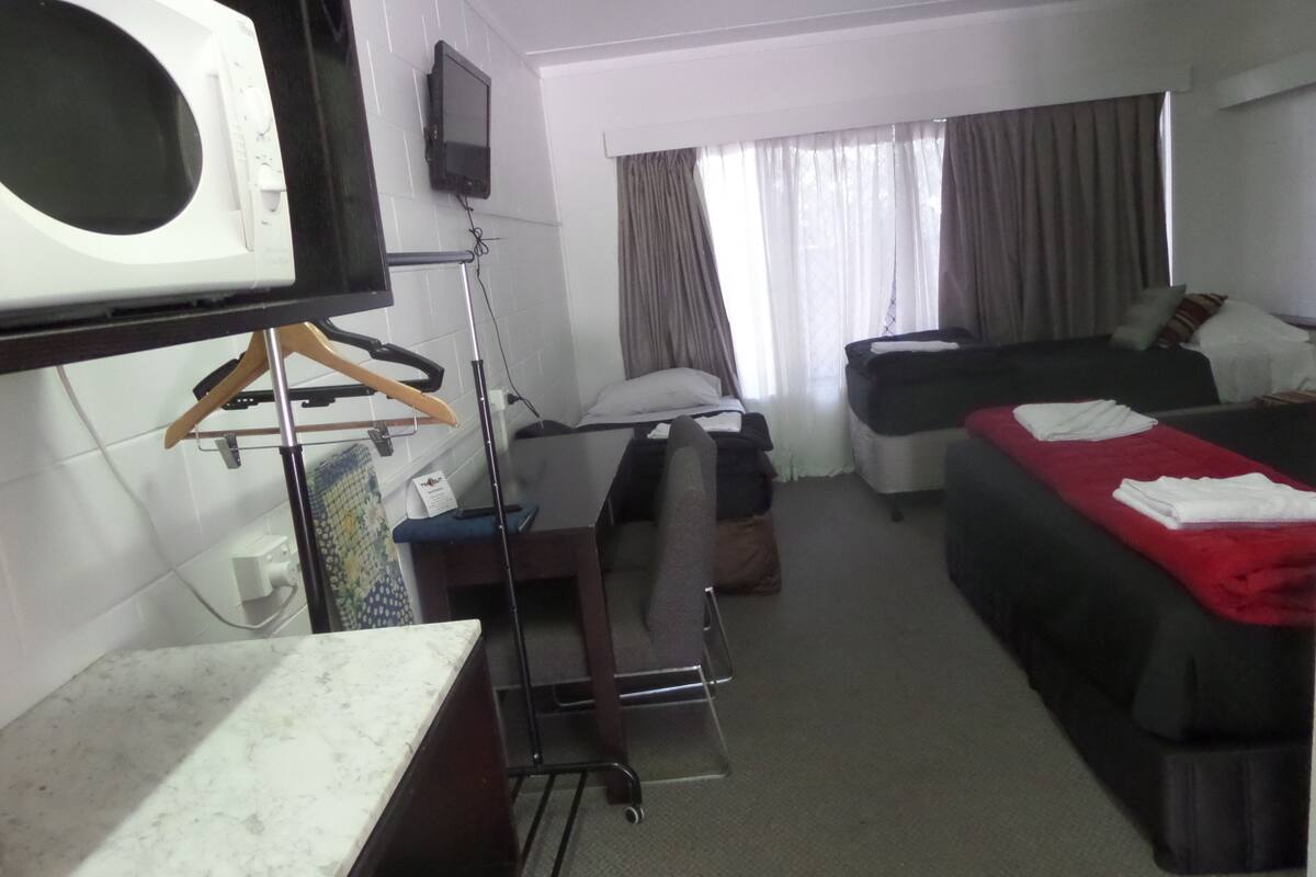 Habitación de hotel con cama, escritorio, silla, televisor montado en la pared y ventana con cortinas.
