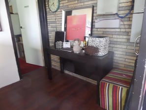 Una habitación con pared de ladrillo, un reloj, una mesita con adornos y un cojín a rayas.