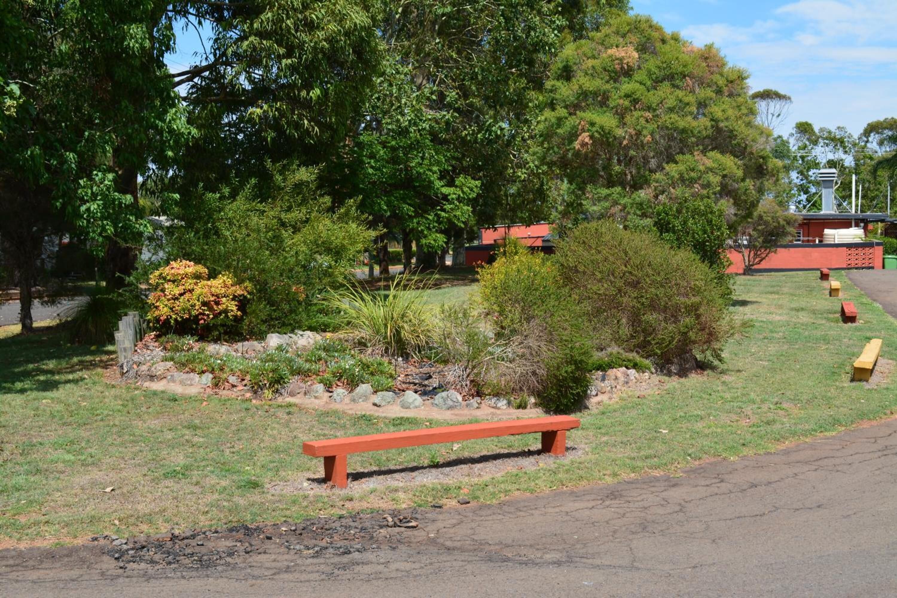 A park with a red bench, trees, and a building in the background.