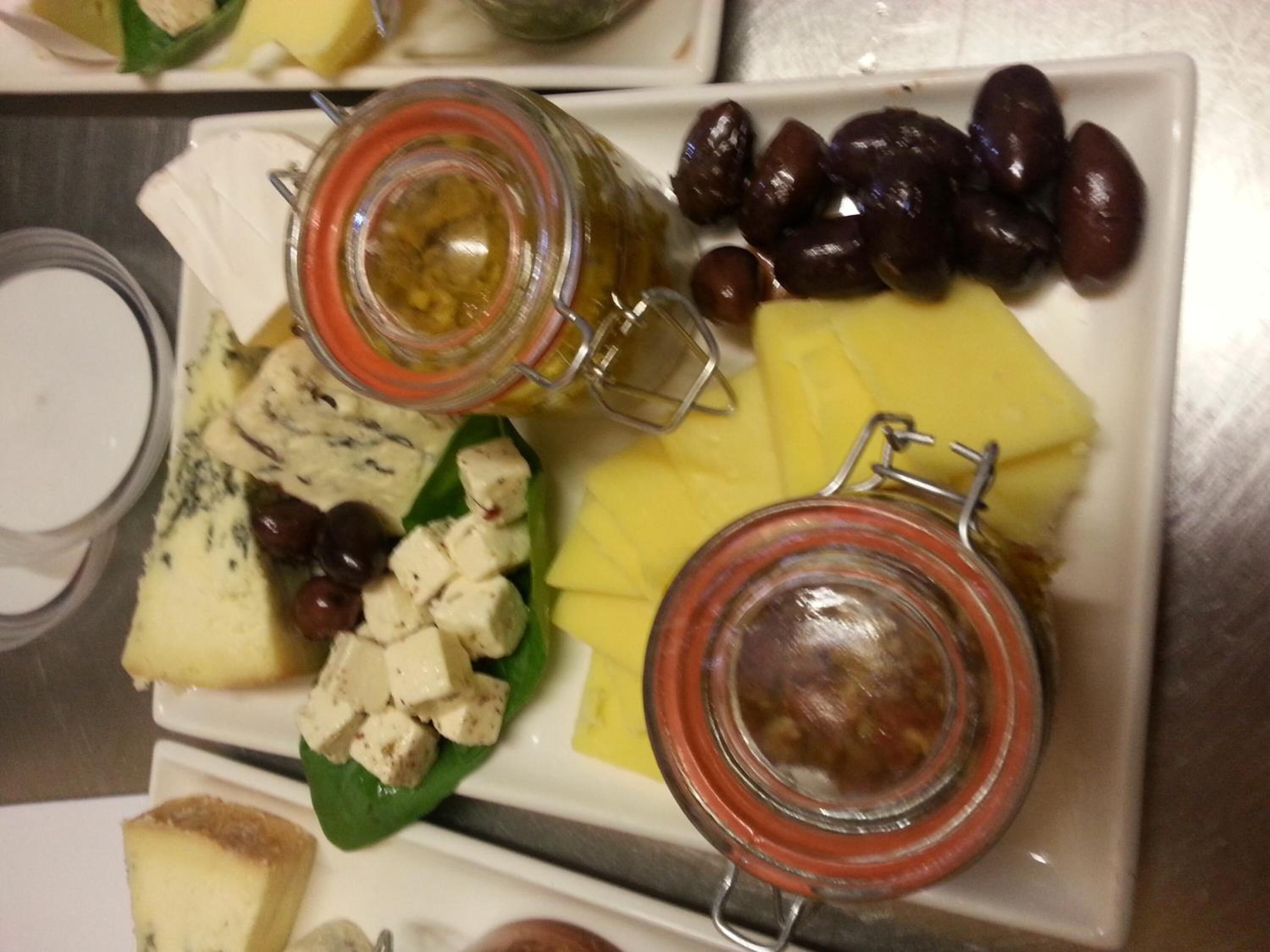 A cheese board with various cheeses, olives, and pickles.