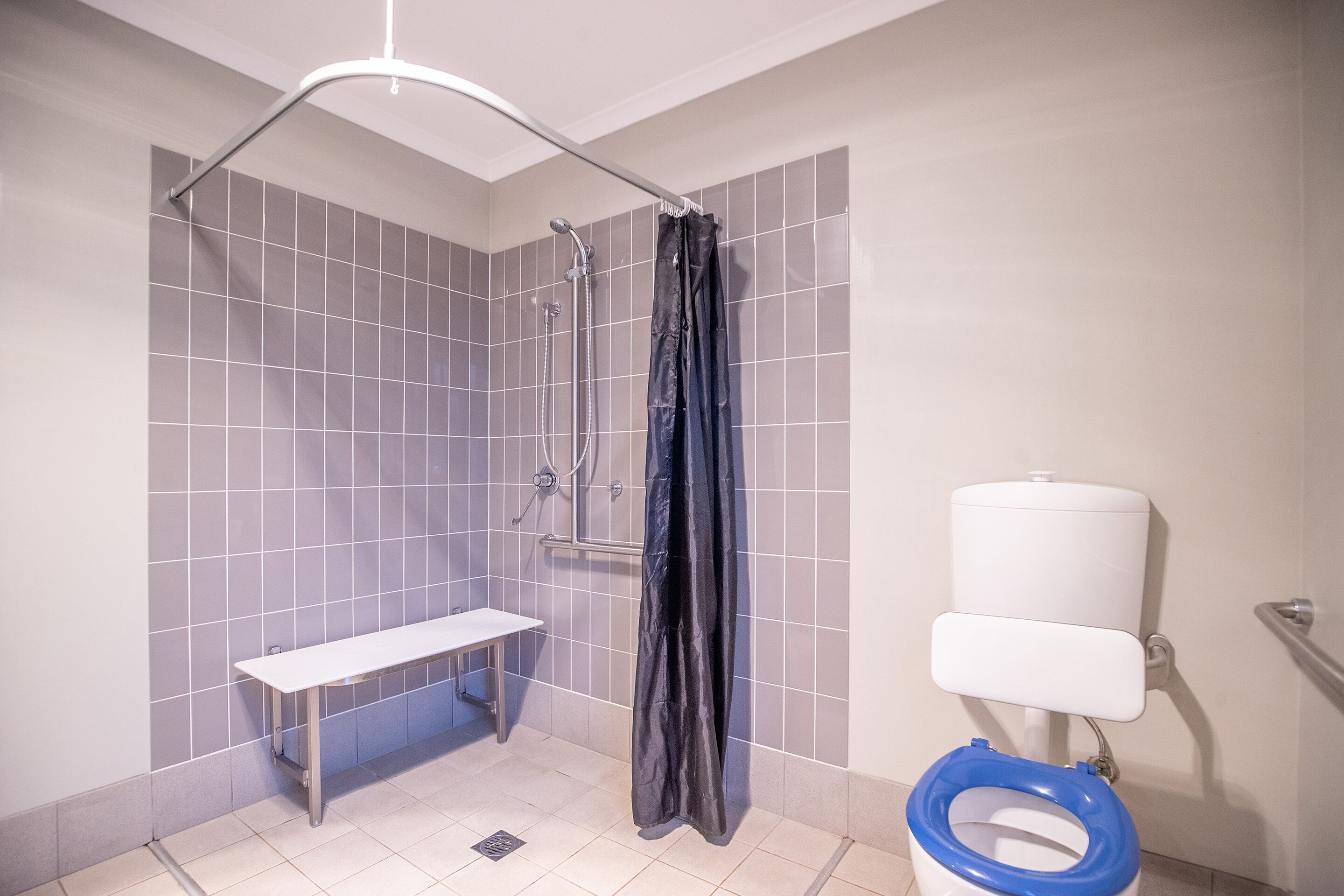A bathroom with a shower, toilet, and bench.