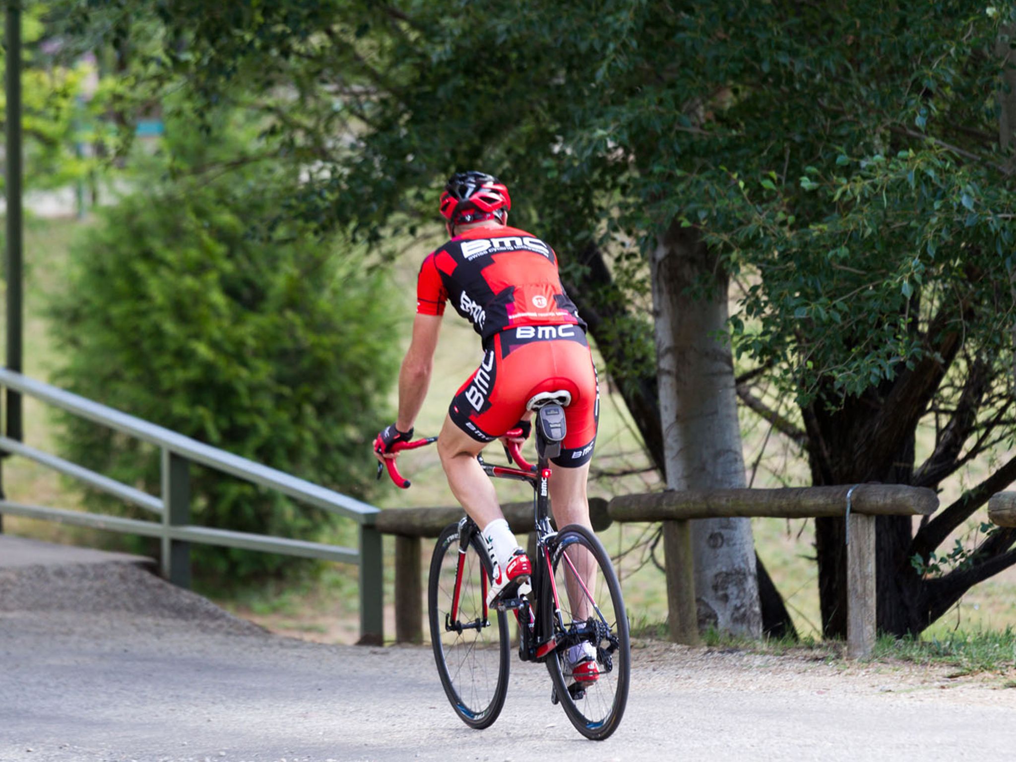 Un cycliste vêtu d’un maillot rouge et noir pédale sur une piste cyclable asphaltée.