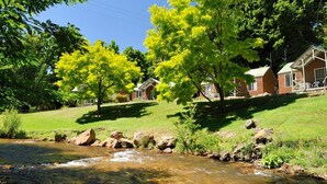 A riverside campsite with cabins, trees, and a grassy area. - NRMA Bright Holiday Park (Bright)