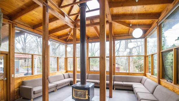 A spacious living room with a large wooden ceiling, built-in wooden benches, and a central wood-burning stove. - NRMA Bright Holiday Park (Bright)