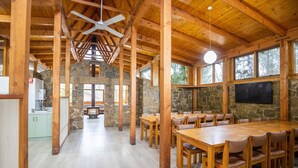A spacious dining area with wooden tables and chairs, stone walls, and large windows. - NRMA Bright Holiday Park (Bright)