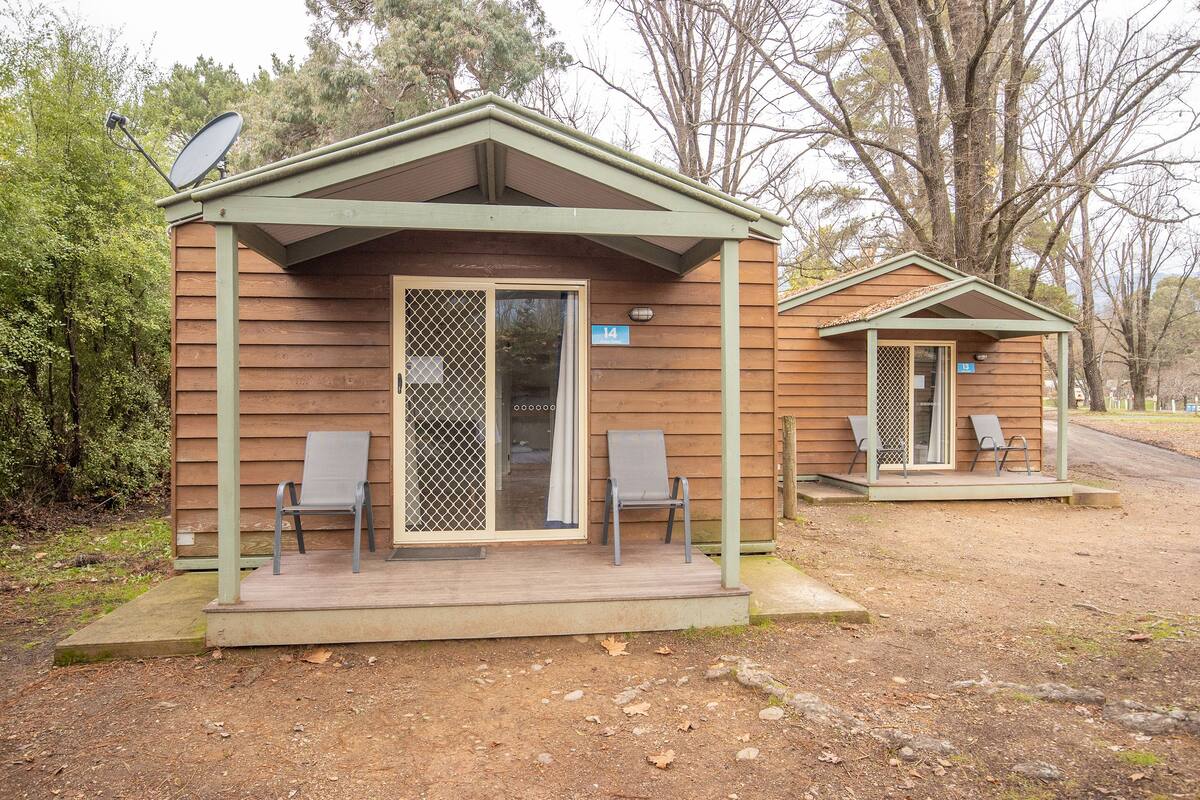 A small wooden cabin with a porch, two chairs, and a satellite dish.
