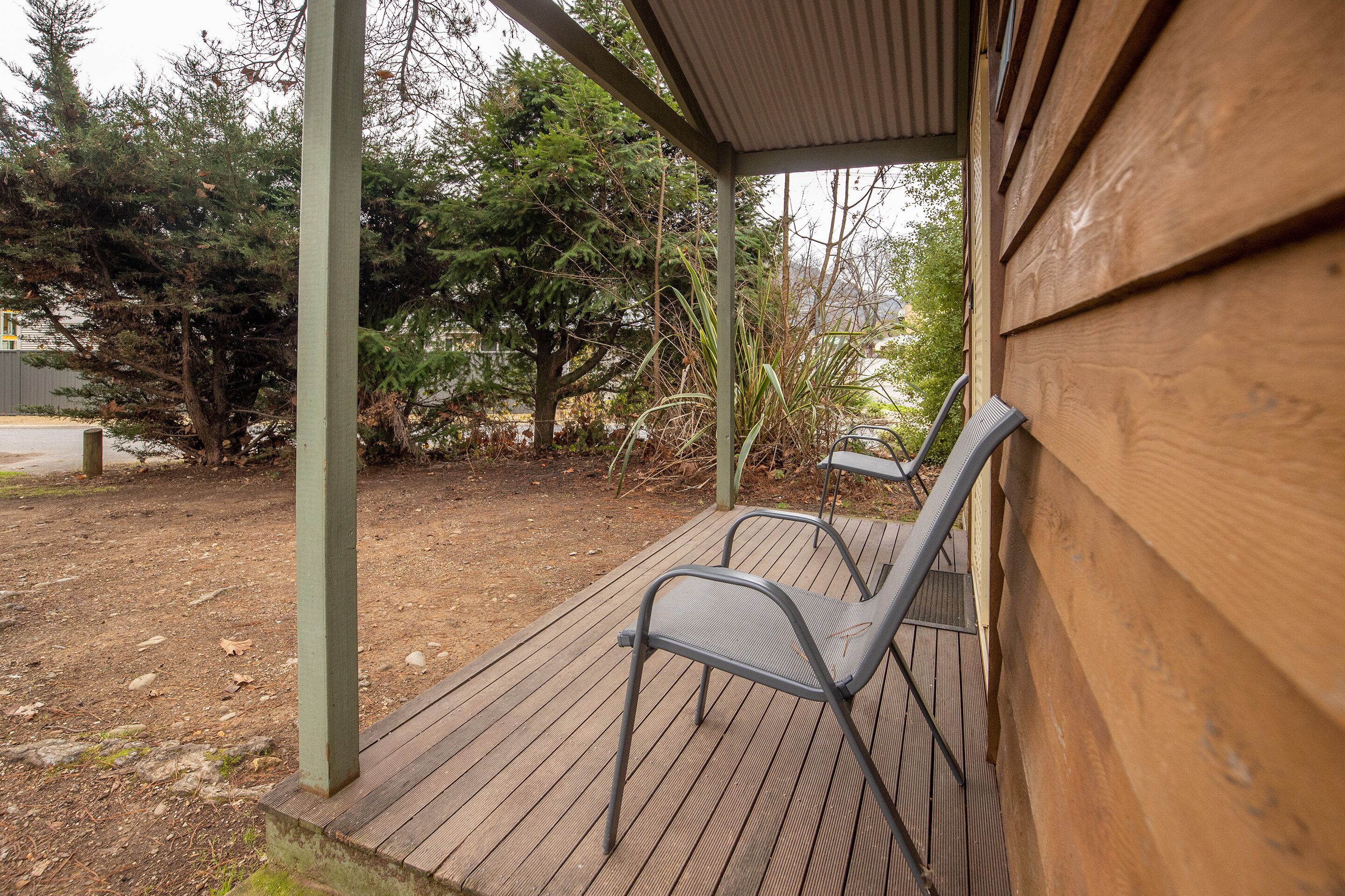 A wooden deck with metal chairs, surrounded by trees and a building.