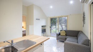 A compact living space with a kitchenette, a gray sofa, and a sliding glass door leading to an outdoor area. - NRMA Bright Holiday Park (Bright)