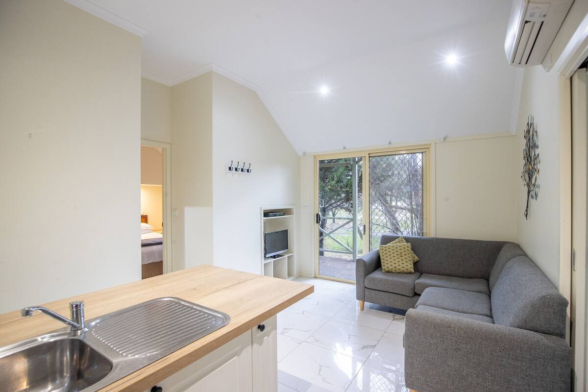 A compact living space with a kitchenette, a gray sofa, and a sliding glass door leading to an outdoor area.
