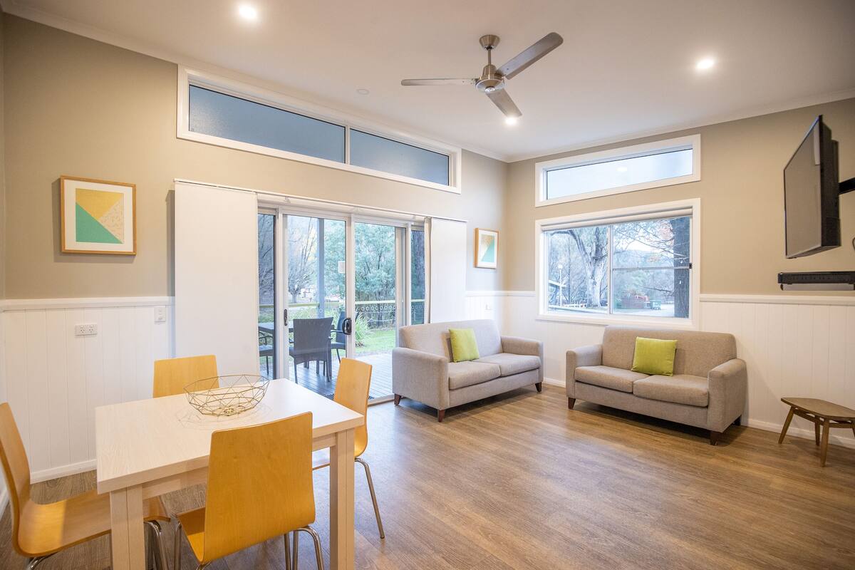 A spacious living room with a dining area, large windows, and a ceiling fan.