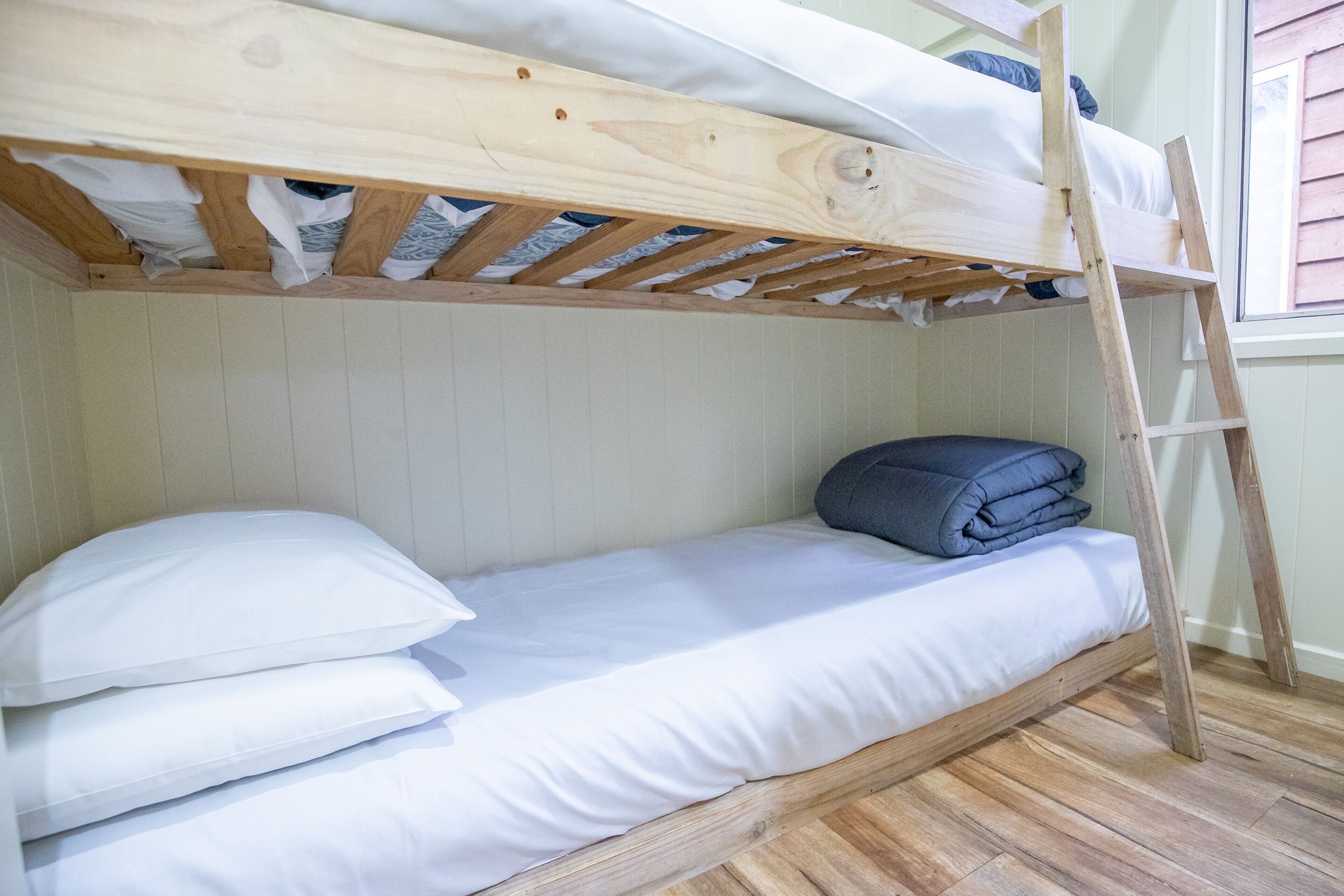 Een stapelbed met witte beddengoed en een houten trap.