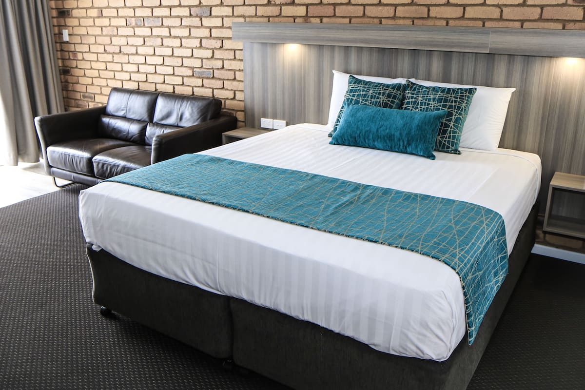 Habitación de hotel con una cama grande, un sillón de cuero y una pared de ladrillo.