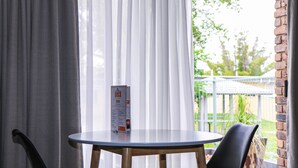 Une table avec un menu, une chaise et une vue sur un mur de briques et de la verdure, le tout visible à travers de fines rideaux.