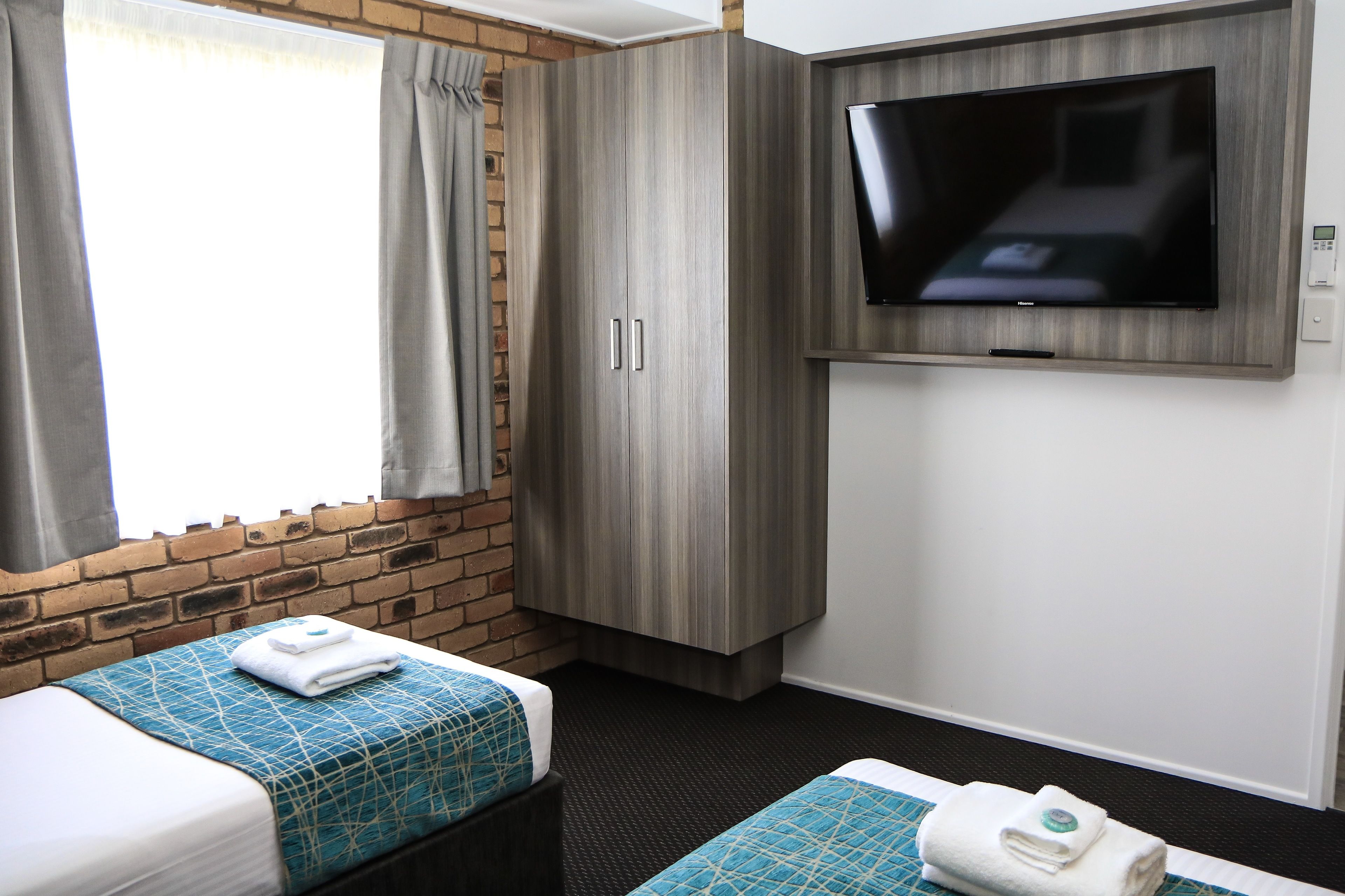 Ein Hotelzimmer mit zwei Betten, einem an der Wand befestigten Fernseher und einer Ziegelwand.