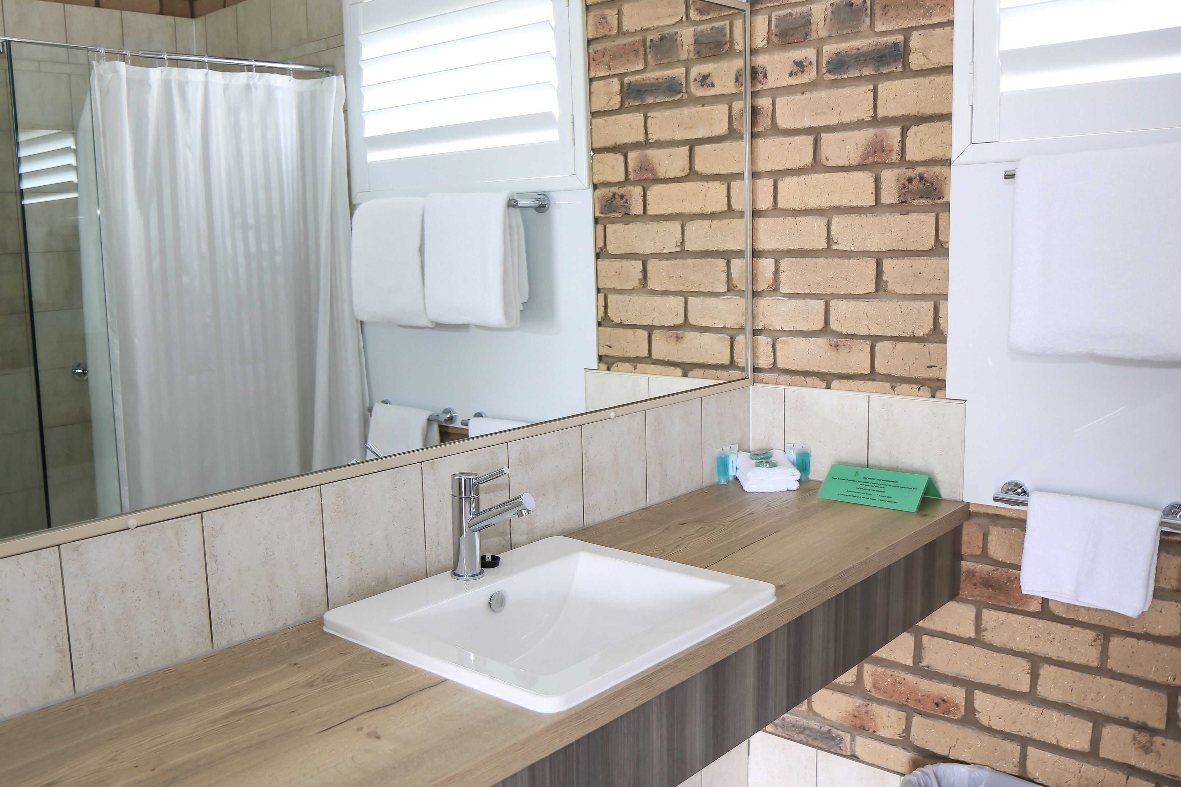 Un baño con lavamanos blanco, cabina de ducha de cristal, espejo y pared de ladrillo.