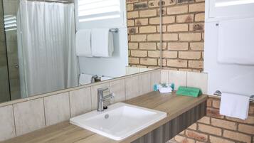Un baño con lavamanos blanco, cabina de ducha de cristal, espejo y pared de ladrillo.