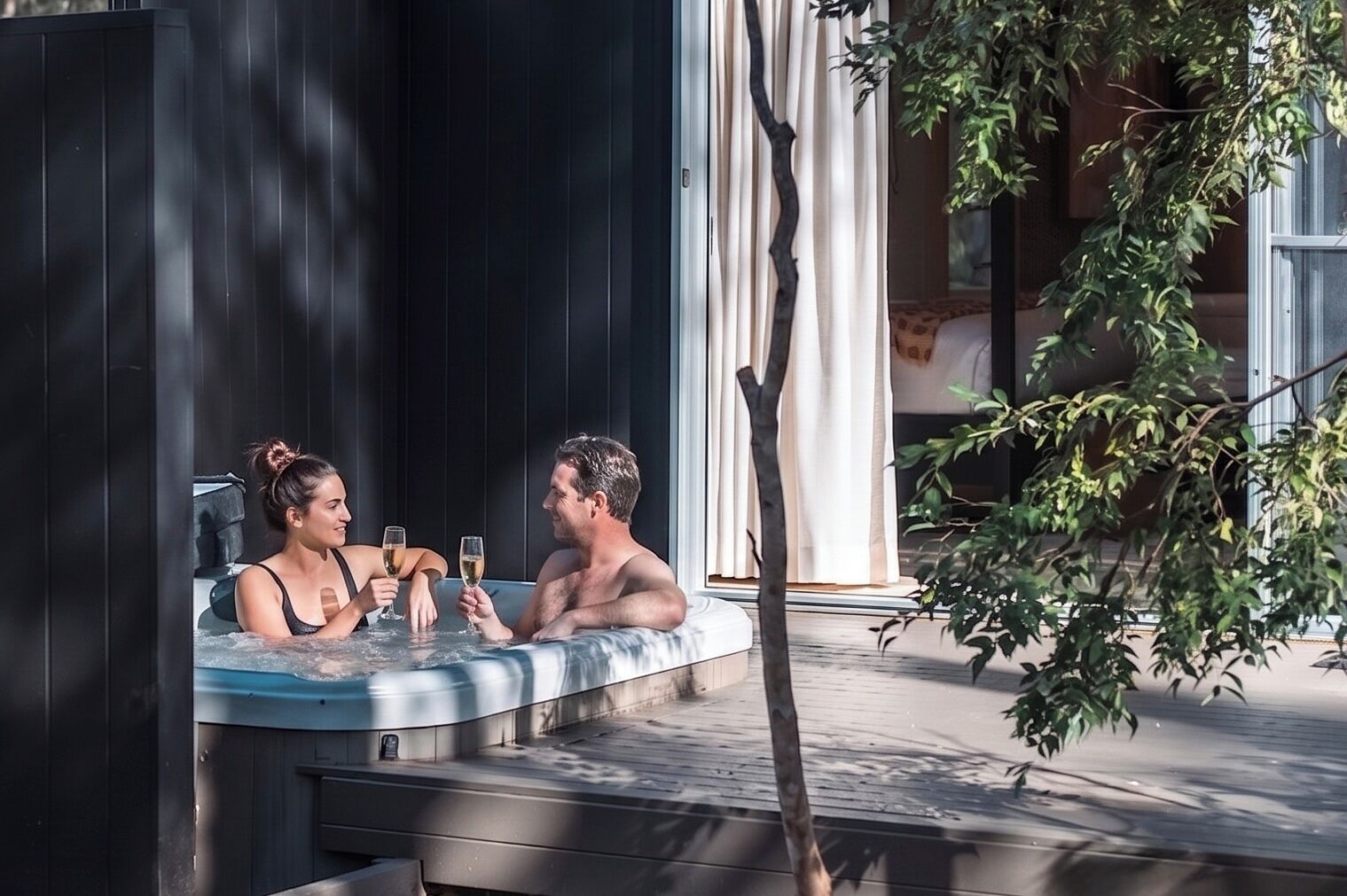 Um casal em uma banheira de hidromassagem, com uma árvore e um edifício ao fundo.