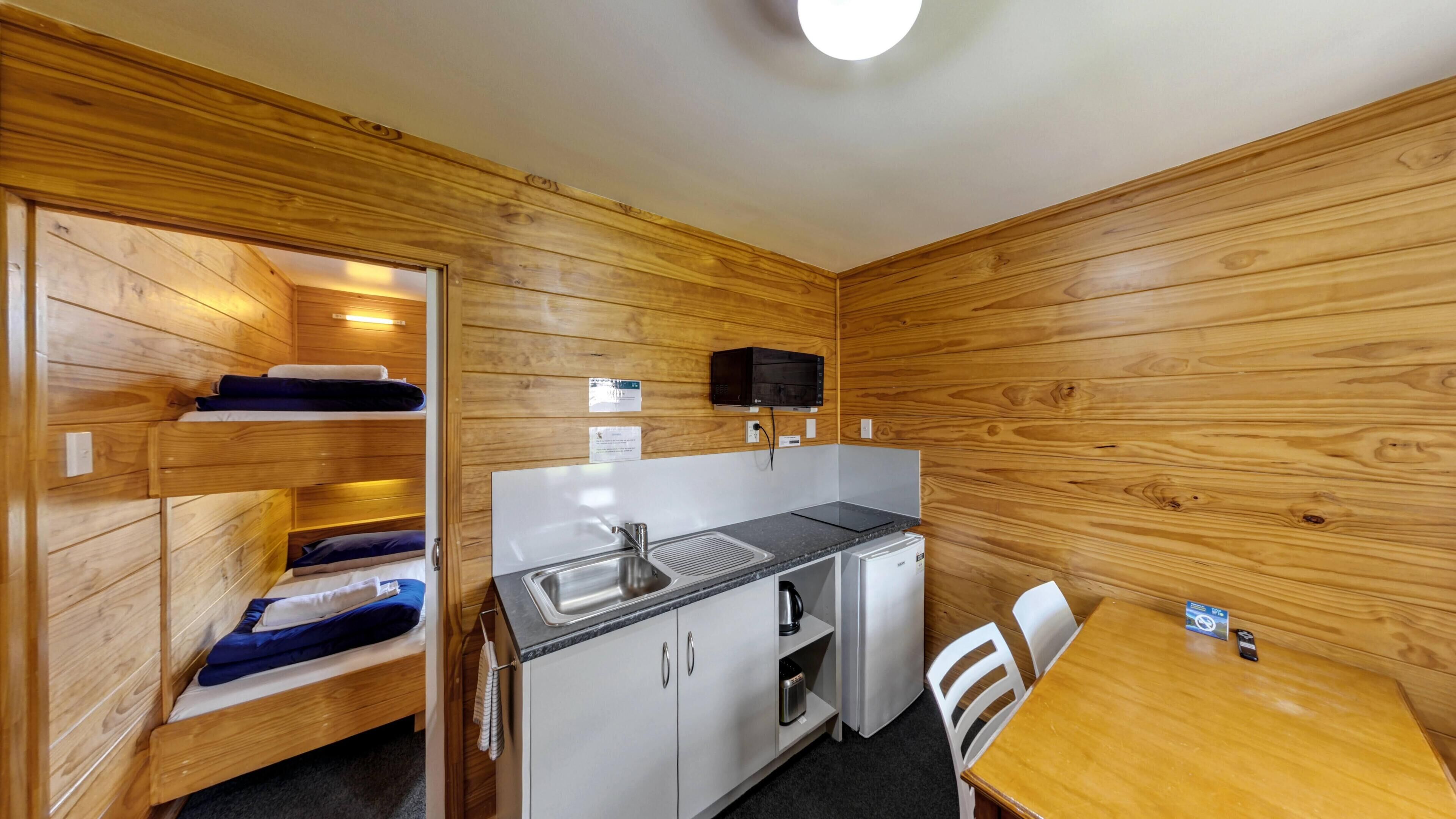 Een compacte kamer met houten wanden, een kitchenette, een bed met blauw beddengoed en een kleine eettafel.