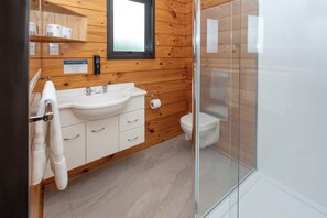 A bathroom with a wooden wall, a white sink, a toilet, and a glass shower enclosure. - Wellington TOP 10 Holiday Park (Lower Hutt)