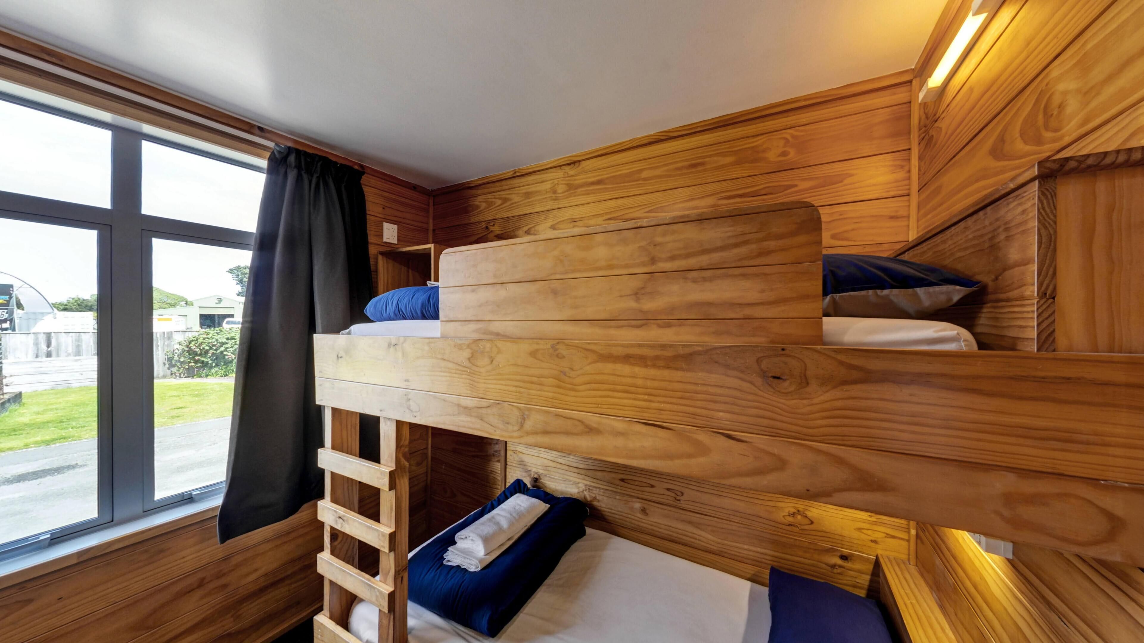 A bunk bed with a ladder, wooden walls, and a window with curtains.