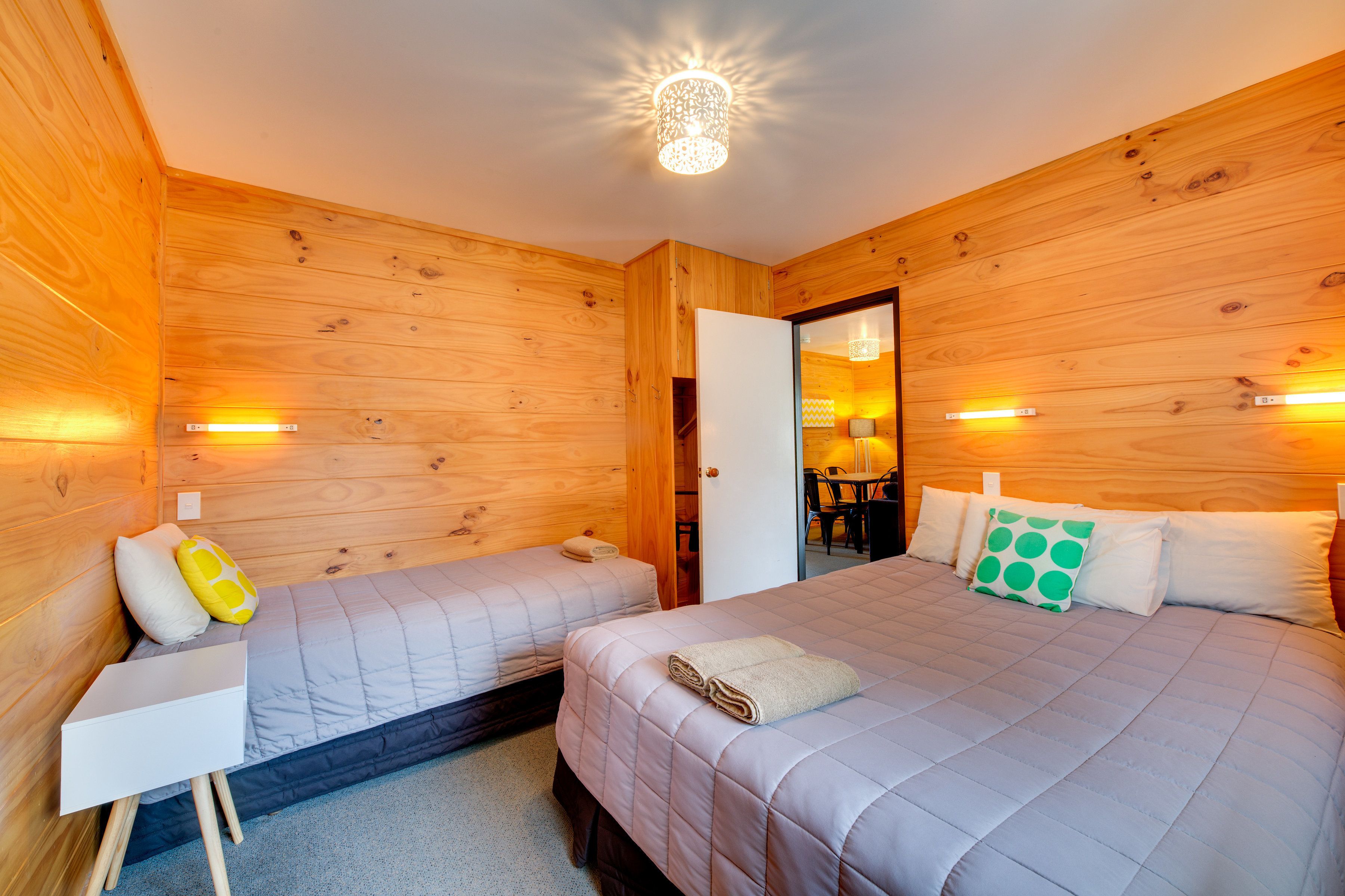 A wooden-paneled room with two beds, a white bedside table, and a mirror.